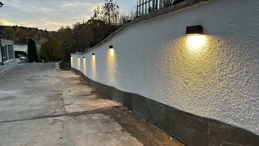 Moderna LED vägglampor monterade längs stödmur i Danderyd vid skymning
